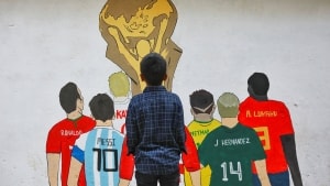 En ung dreng i Dhaka I Bangladesh kigger på fodboldstjernerne. Sporten forbinder milliarder af mennesker på kryds og tværs af verden, og intet er større end VM. Men organisationen bag, Fifa, har i mange år ageret som et forbrydersyndikat, der gemte sig bag skønheden af deres turnering, mener mange kritikere. I denne artikel kigger Avisen Danmark på fodboldens skyggesider. Foto: Mohammad Ponir Hossain 