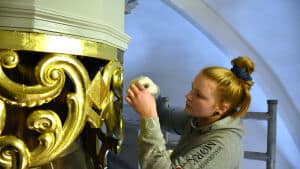 Det er ikke nogen helt almindelig opgave, malerlærling Katrine Skau her er i gang med. Hun lægger bladguld på udskæringerne omkring orglet. Det er en lille del af restaureringen af Sct. Nicolai Kirke. Foto: Leif Baun